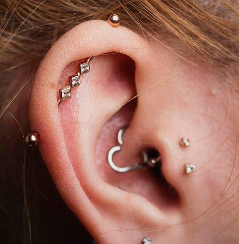 Cartilagem perfurada no ouvido de uma rapariga com anel de brinco, prego, corrente
