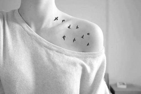 女孩锁骨上的纹身。素描，妇女的字母，图案，鸟，花，星星