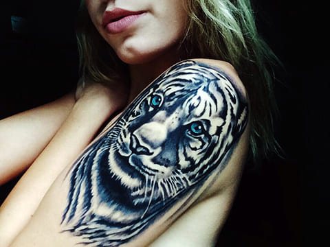 Tetoválás egy kék szemű tigrisről egy lány vállán