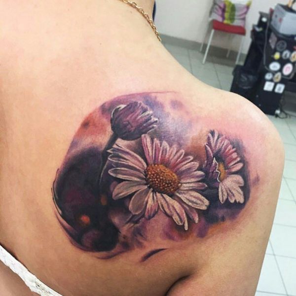 Tatuagem estilo realismo de três margaridas na omoplata de uma rapariga