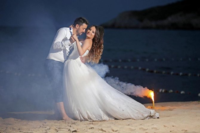 Булката и младоженецът танцуват на плажа през нощта.
